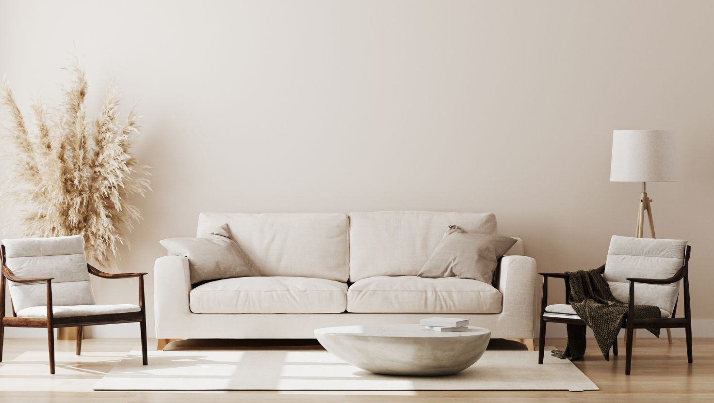 Salon w stonowanych barwach z beżową sofą, dwoma drewnianymi fotelami, nowoczesnym stolikiem kawowym, trawą pampasową w wazonie i minimalistycznymi dekoracjami na jasnym dywanie na kremowej ścianie — idealny do relaksu i zastanowienia się nad sposobami ogrzewania domu.